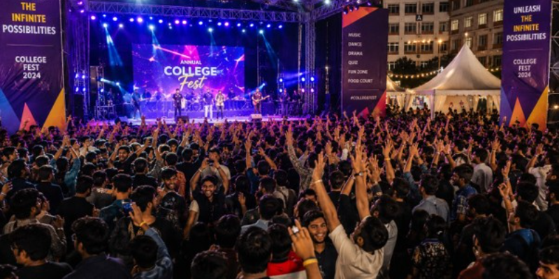 Wide shot of an energetic Indian college fest scene with students cheering, colorful stage lighting, banners, and a crowd, evening atmosphere, dynamic event photography style